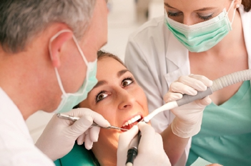 Female patient opens wide as a dentist and hygienist work on her teeth.