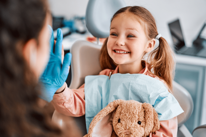 A young girl smiles at the dentist while holding a stuffed animal.