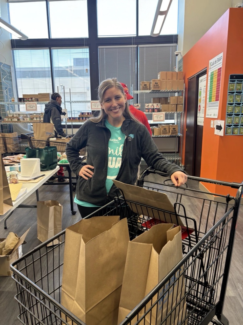 woman smiling wearing hudec dental shirt next to grocery cart with brown bags