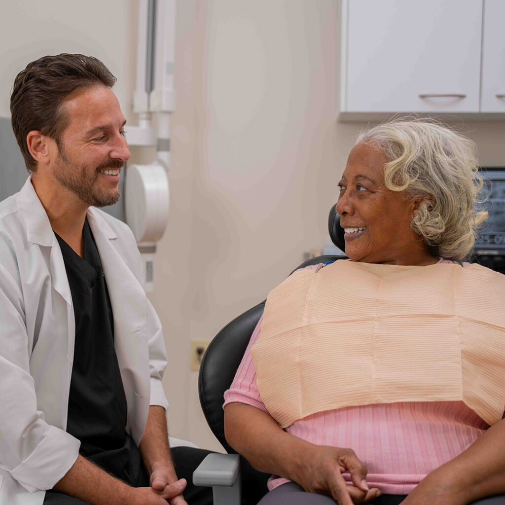 Dentist smiling while speaking with an older patient seated in a dental chair