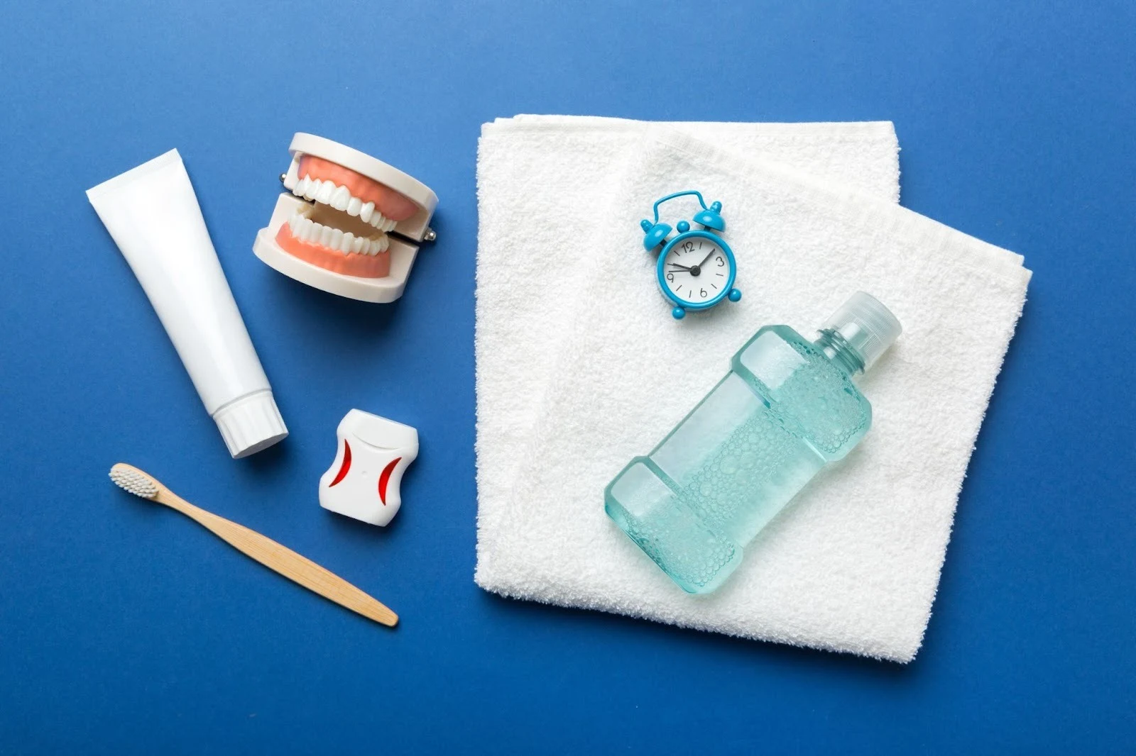 Flat lay of oral hygiene items including a toothbrush, toothpaste, dental floss, mouthwash, and a dental model on a blue background.