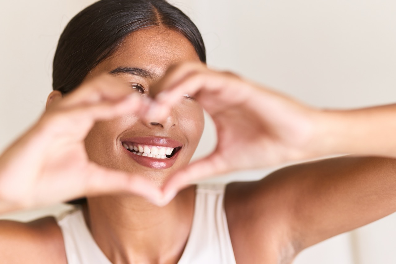 Woman smiling making a heart shape with hands - The connection between oral health and heart health