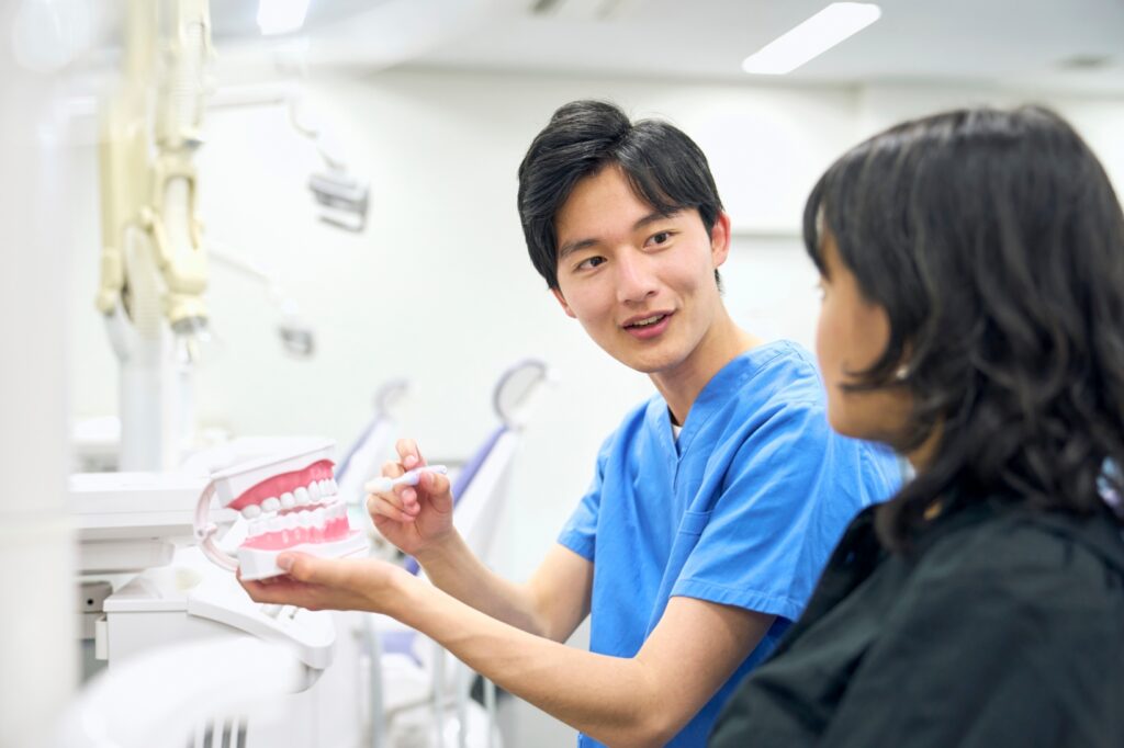 A dentist using a model of teeth to demonstrate the proper tooth brushing technique to a student